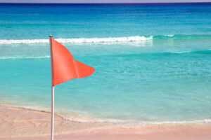 Red flag on a beach with the ocean in the background. 