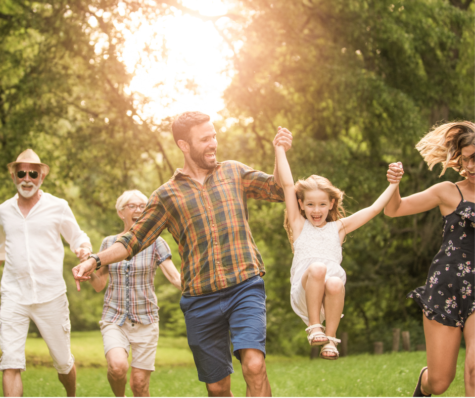 Multi-generational family walking in a grassy area, swinging daughter, having fun together.